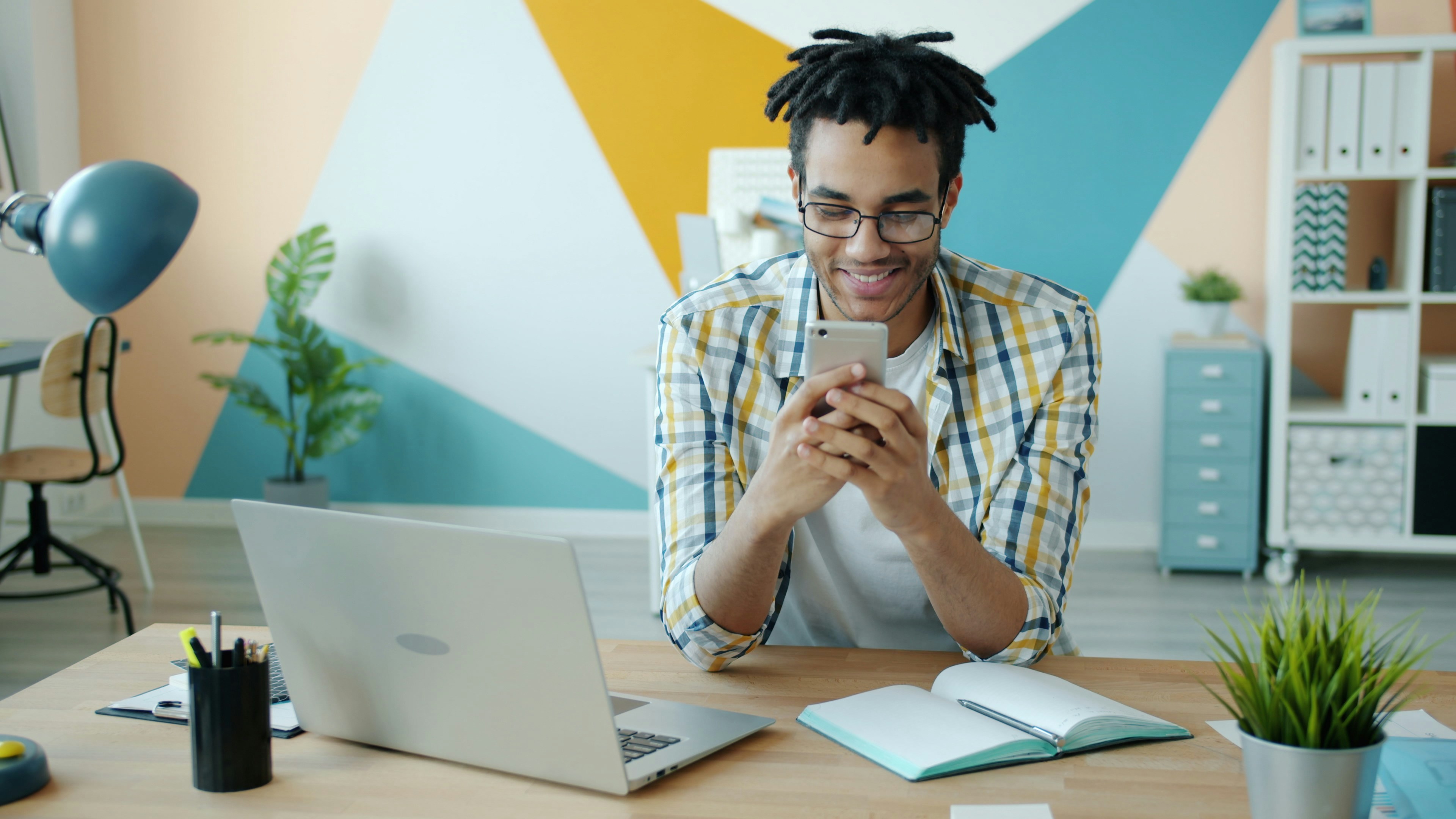 Slow motion of cheerful African American guy enjoying smartphone activities in workplace touching screen and smiling. People and modern devices concept.